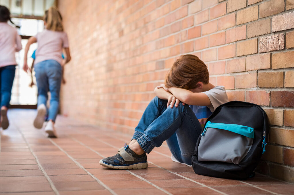 A child hides their face while sitting in a school hallway. Learn how a trauma therapist can offer support with healing from childhood trauma. Search “find a trauma therapist near me” to learn more.
