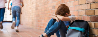 Photo of a young boy sitting against a wall looking sad. This photo represents how understanding childhood trauma can help parents recognize it in children.